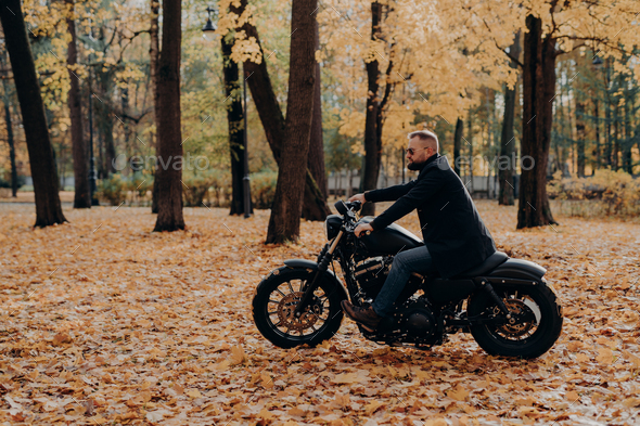 Fashionable male motorcycle driver poses on black motorbike, wears  protective sunglasses Stock Photo by StudioVK