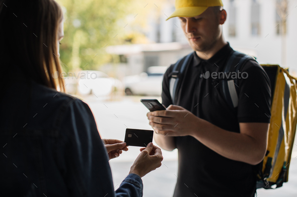 Cropped view of hands of caucasian delivery man and young woman at the door, pay by card for order