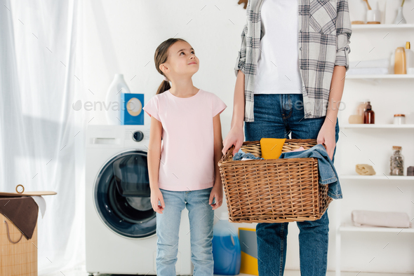 daughter in pink t-shirt looking to mother in grey shirt with basket in laundry room