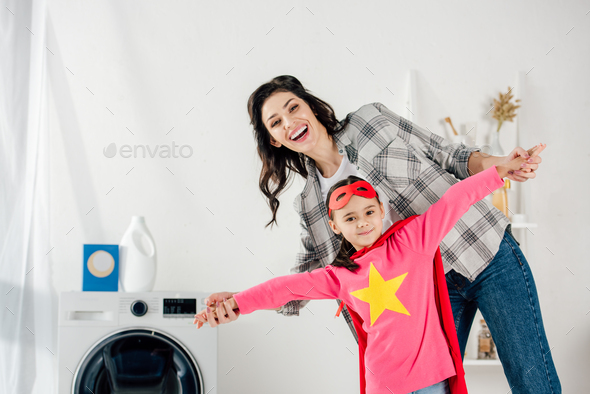 mother in grey shirt and daughter in red homemade suit with star sign having fun in laundry room