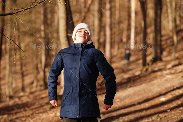 Young boy wear jacket and hat in early spring forest. Inhale fresh air to the fullest.