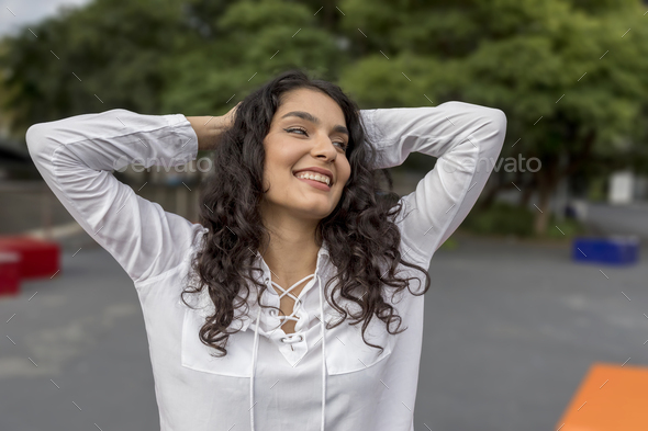 Black hair woman hands over head looking at side sitting outdoor