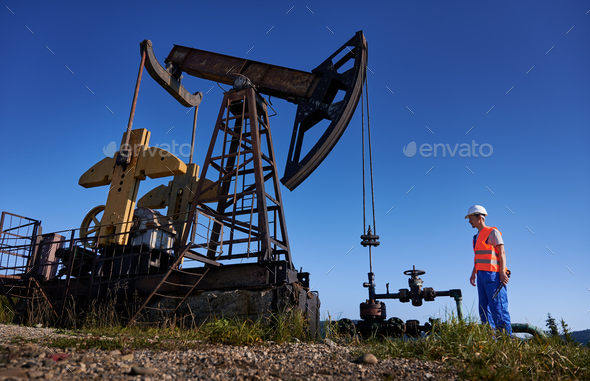 Engineer controlling operation of petroleum rig under blue sky.