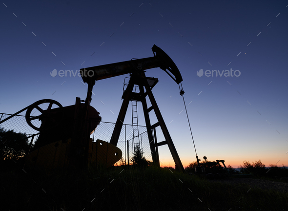 Oil field with petroleum pump jack under beautiful night sky.
