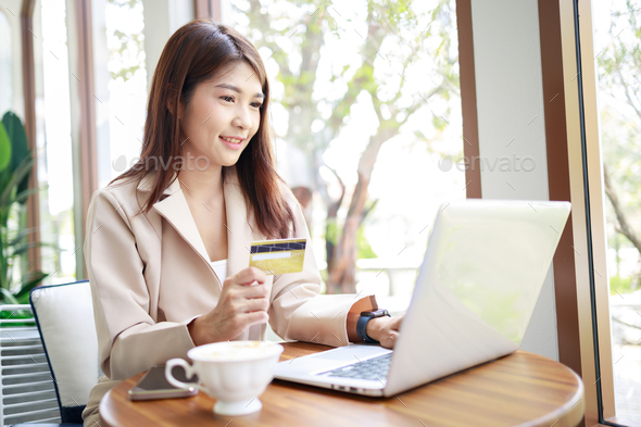 Asian woman use a credit card for goods payments shopping online by laptop. business concept.