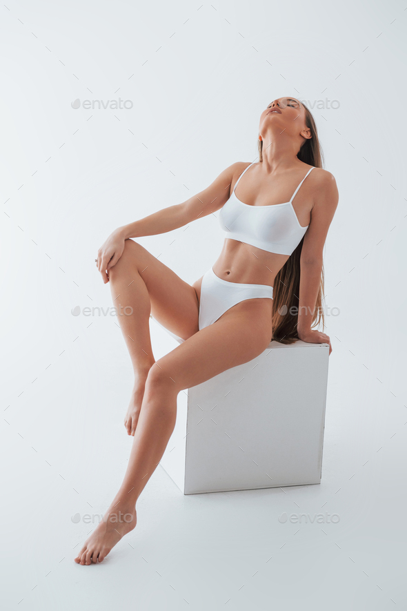 Sitting on white cube. Woman in underwear with slim body type is posing in  the studio Stock Photo by mstandret