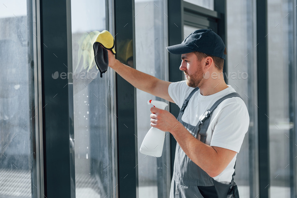 Cleaning window by using special liquid. Repairman is working indoors in the modern room