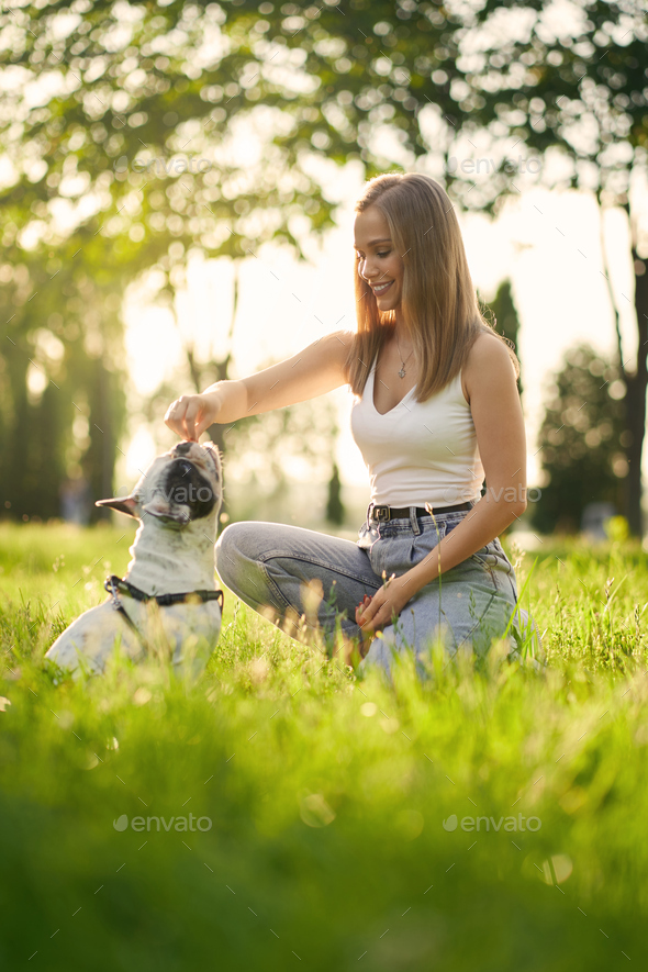 Young smiling woman training french bulldog in park.