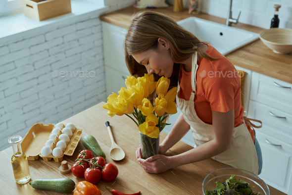 Top view of beautiful young woman smelling tulips while cooking at the domestic kitchen