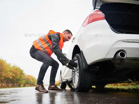Emergency auto mechanic changing flat tire on the road.