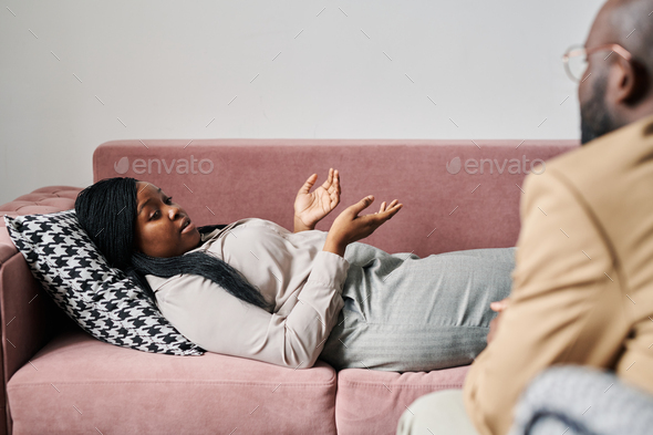 Young stressed female patient lying on couch and describing her problem