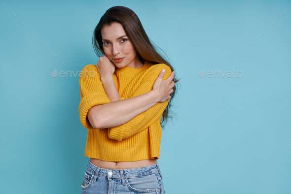 Beautiful young woman hugging self while standing against blue background