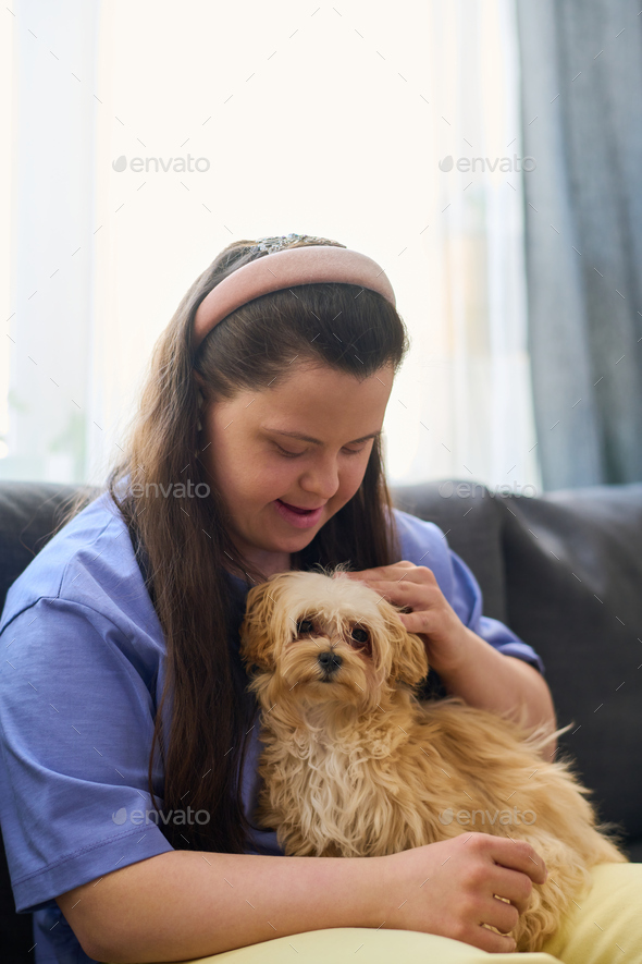 Happy girl with Down syndrome cuddling fluffy dog sitting on her knees
