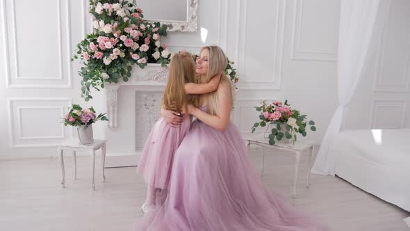 Child daughter congratulates hugging kissing happy young mom in white room. Happy mother's day
