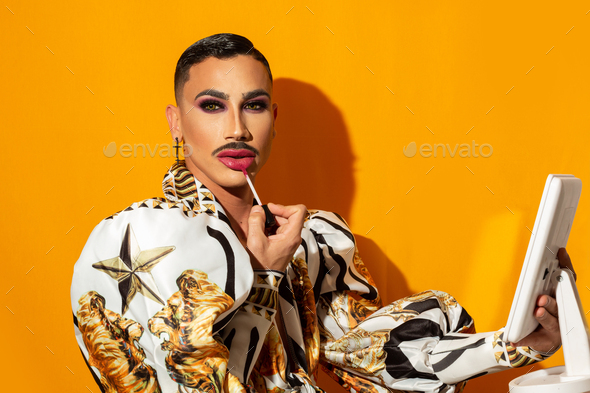 Portrait of drag queen with mustache painting lipstick on yellow background