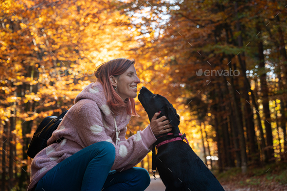 Happy smiling young woman kneeling down to cuddle her cute black labrador puppy
