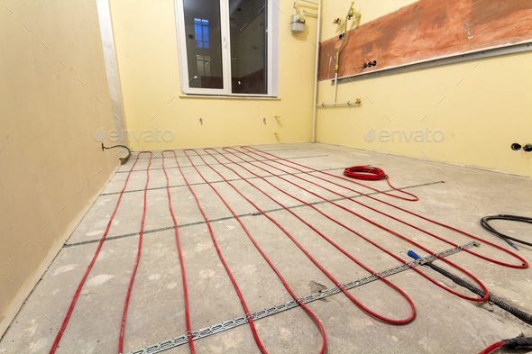 Heating red electrical cable wire installation on cement floor in small new unfinished room with