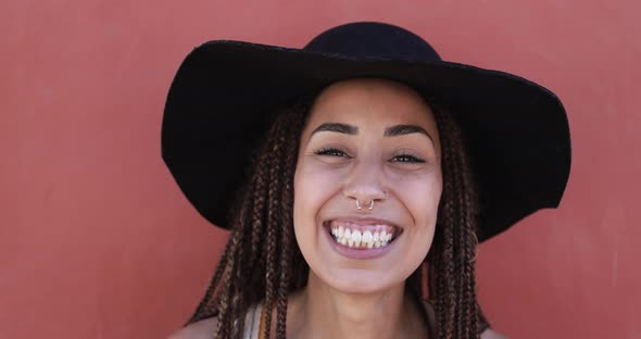 Young african hipster woman with braids laughing on camera while wearing hat alt