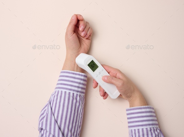 Process of measuring body temperature on the wrist with a non-contact thermometer, beige background