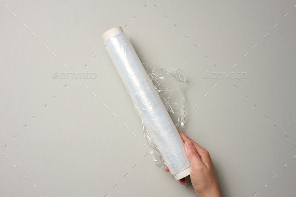 Two female hands hold a roll of transparent cling film for packaging products, gray background