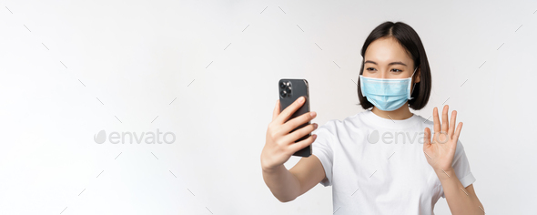 Health and covid-19 concept. Modern asian girl, student in medical mask, video chat with mobile