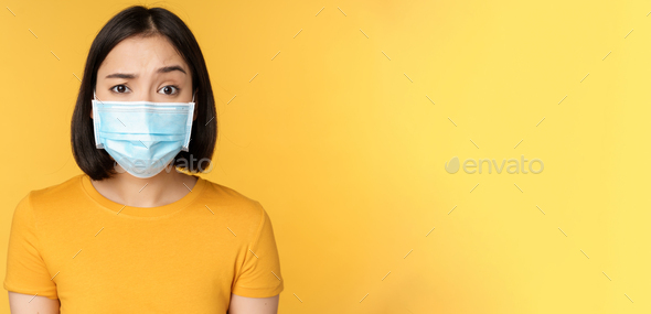 Portrait of skeptical and confused asian woman in medical face mask, raising eyebrow doubtful
