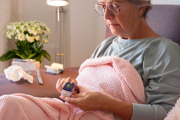 Elderly caucasian woman with cough and fever as seasonal flu or pollen allergy sitting on sofa