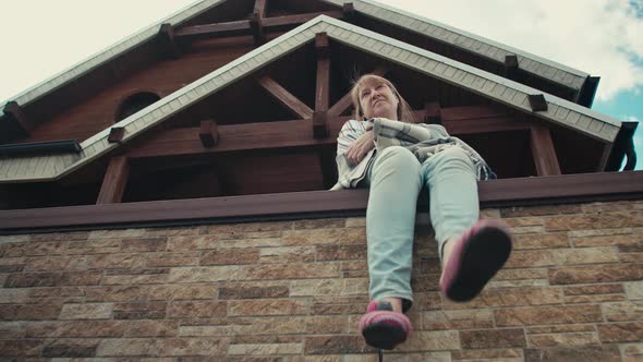 An adult caucasian woman sits covered with a plaid on the terrace of a country house alt