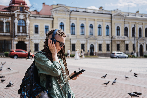 Hipster woman traveler with dreadlocks headphones and cell phone use audio guide