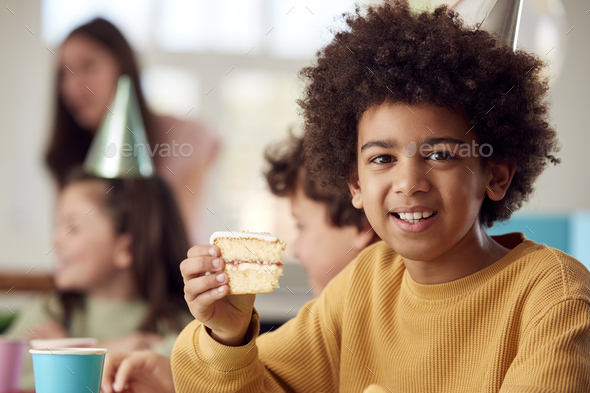 Portrait Of Boy Eating Birthday Cake At Party With Parents And Friends At Home