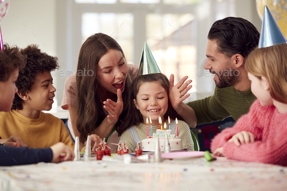 Girl With Candles On Birthday Cake At Surprise Party With Parents And Friends At Home