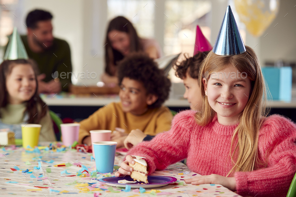 Portrait Of Girl Eating Birthday Cake At Party With Parents And Friends At Home