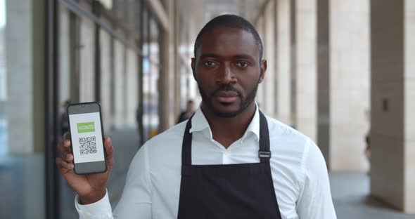 Medium Shot of African Man in Apron Showing Smartphone with Vaccination Certificate alt