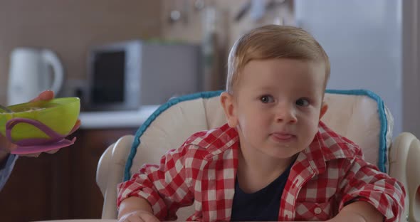 Portrait of Cute Child Not Wanting To Eat Food And Mother Trying To Feed Baby Boy alt