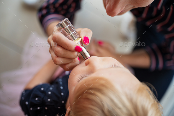 Mother putting lipstick on toddler daughter lips