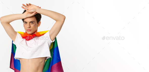 Beautiful Gay Man With Glitter On Face Wearing Crop Top And Rainbow Lgbt Flag Posing Against