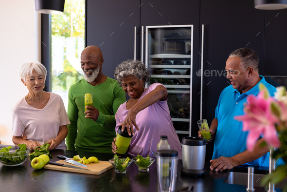 African american senior woman making smoothie for multiracial friends on kitchen counter