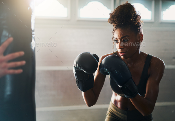 african woman boxing with punching bag in garage gym