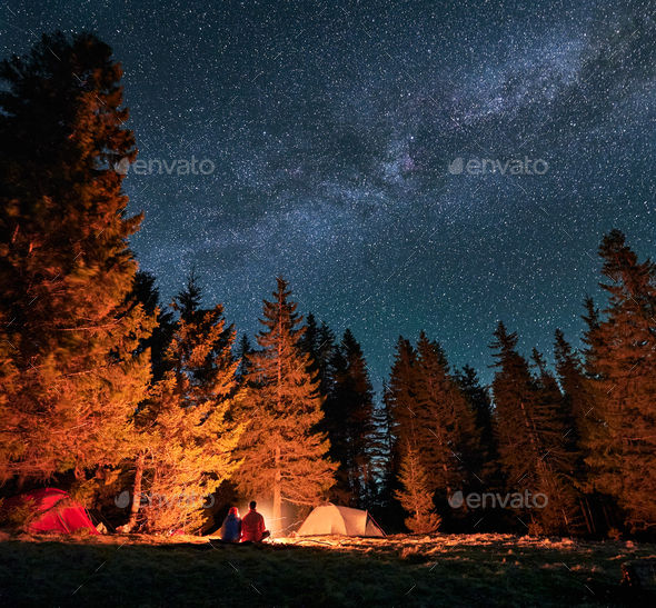 Man and woman resting in campsite at starry evening outdoors.