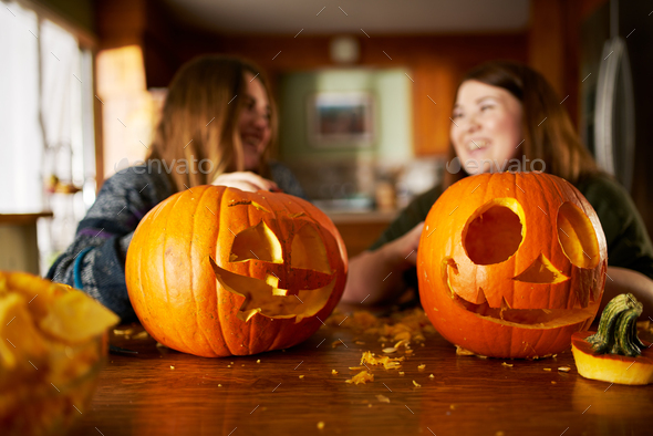 sisters showing off finished jack-o-lanterns they just made, selective focus on pumpkins