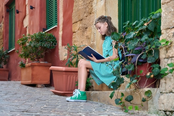 Pre-adolescent schoolgirl with a book sitting on steps of outdoor