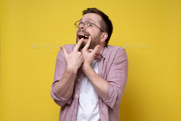 Man in glasses and casual clothes opened his mouth and shows a missing tooth with fingers