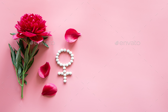 Gender Venus symbol made of pills, and peony flower on a pink background.