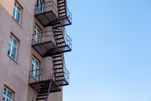 Silhouette of a fire escape on a high-rise building against a blue sky with clouds