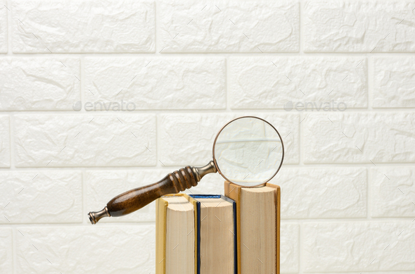 Wooden magnifying glass lies on a stack of books, new knowledge and discoveries are reading books