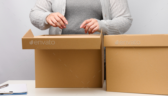 Woman in gray clothes stands and holds open brown box on a white background