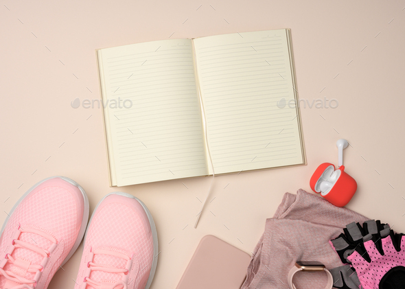 Open notebook with blank pages, pink sneakers and smart gadgets on a beige background.