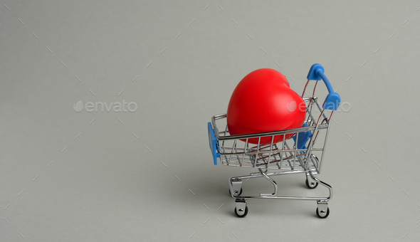 Red heart in a miniature metal trolley from the store on a gray background.
