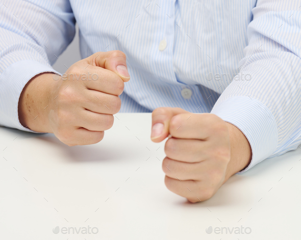 Two female hands folded into a fist on a white table. Strict leader, aggression