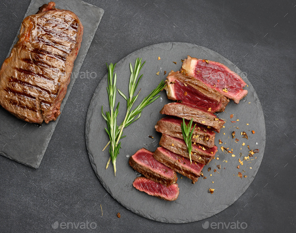 Fried beef steaks cut into pieces on a black board, the degree of doneness rare with blood